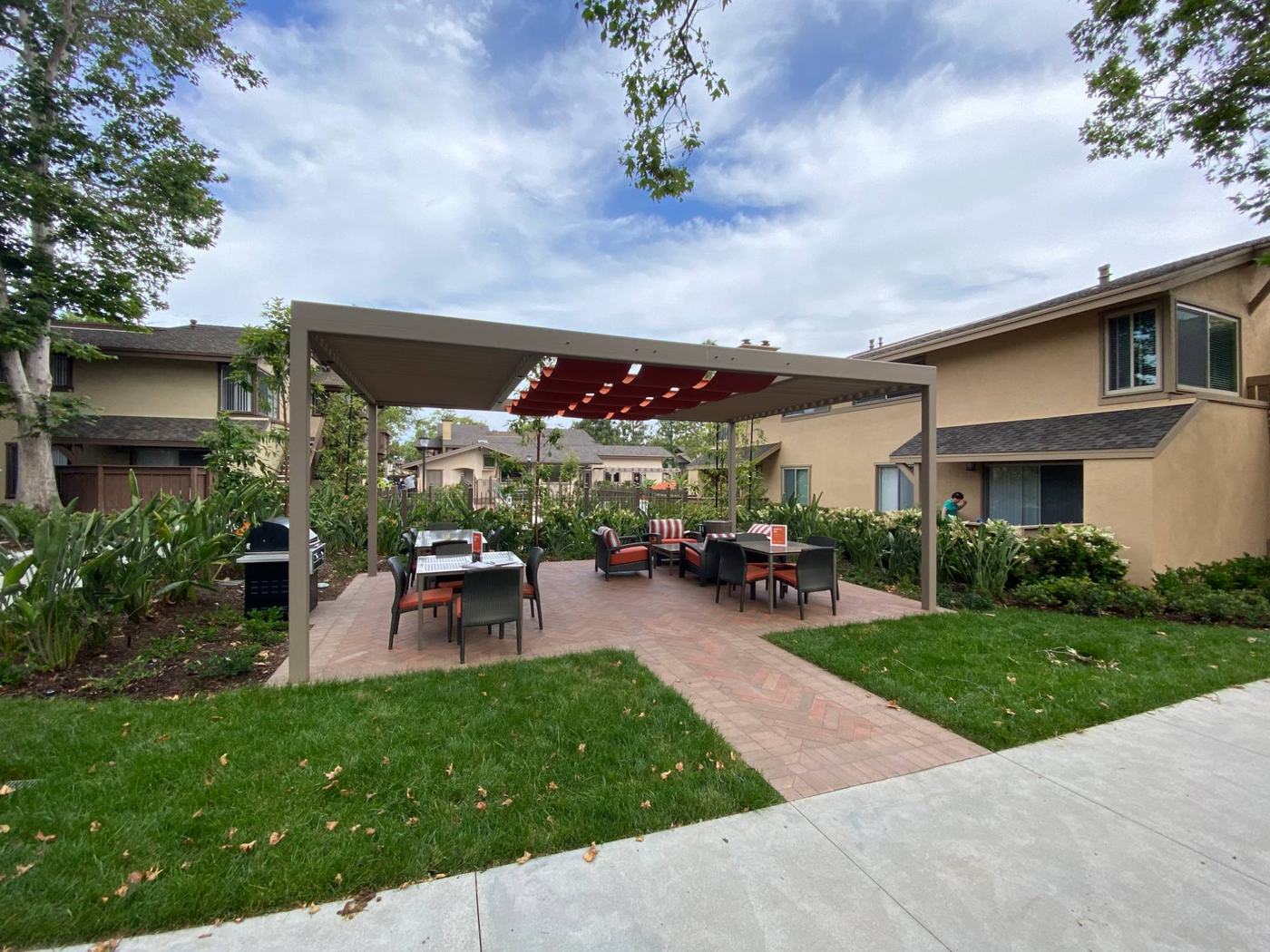 Renovated common-area patio with pergola shade structure, outdoor furniture, and paver hardscape at a residential property